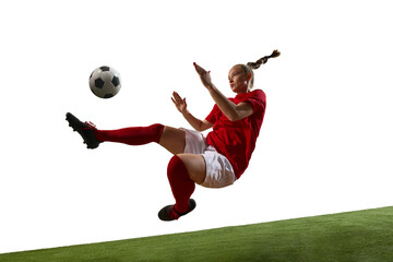 Female football player jumping high for powerful kick with tense focused face on green grassy...