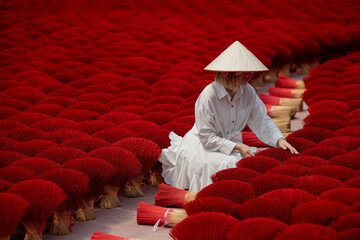 Female asian adult in traditional hat amidst vibrant incense sticks in Vietnam travel scene