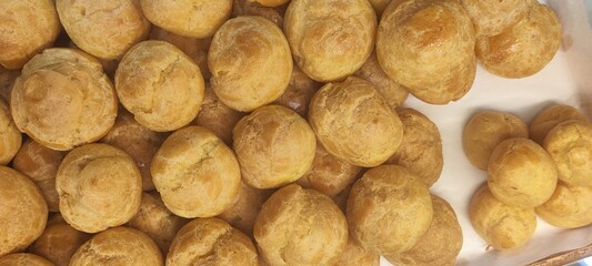 Top view of a batch of golden-brown cream puffs arranged closely on a tray. Light, airy pastry shells made from choux dough, often filled with cream. Ideal for bakery, dessert, and pastry-related