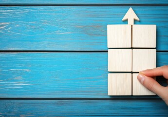 Light-colored wooden blocks arranged in a grid formation on a teal wooden surface.  A hand touches a block. An arrow points upwards