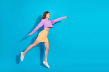 Fashionable young woman poses dynamically in trendy outfit against bright blue background, expressing energy and style