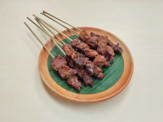 Satay or sate, Indonesian dish of seasoned skewered and grilled meat served with a sauce on wooden plate, high angle view