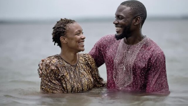 A newly baptized couple, embracing and smiling joyfully as they emerge from the water, symbolizing their shared commitment to living a Christian life together.