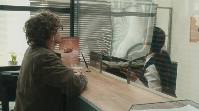 Female bank teller assisting male client with filling out documents checking customers passport at service window
