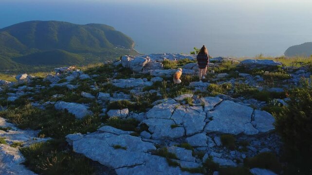 Woman Hiking with Dog on Rocky Mountain Overlooking Sea at Sunset Aerial Scenic Nature Travel Shot