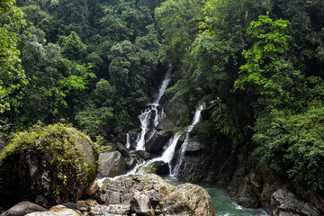 Tiered waterfall surrounded by lush green trees and rocks in Meghalaya. 