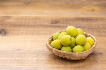 竹かごに盛られた新鮮な青梅と木目テーブル