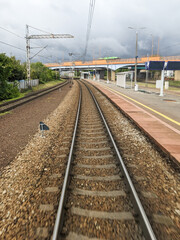 Fototapeta premium Curved railway tracks leading out of a modern train station, captured from the rear of a moving train under dramatic stormy skies — symbolizing travel, transition, and the power of modern rail infrast