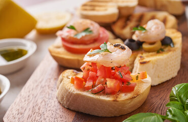 Olives, oil, Grilled shrimps and fresh vegetable salad on a wooden board on black slate stone board over dark background, juicy tomatoes on fresh bread, pesto as topping. top view. Flat lay