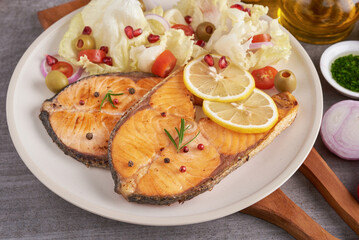 Delicious cooked salmon fish fillets. Grilled salmon fish fillet and fresh green lettuce vegetable tomato salad. Balanced nutrition concept for clean eating flexitarian mediterranean diet.