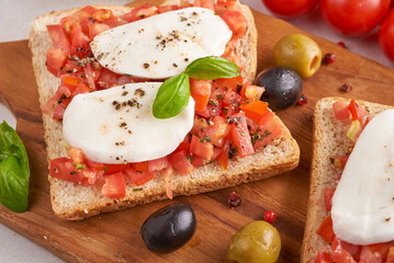 Bruschetta with tomatoes, mozzarella cheese and basil on a cutting board. Traditional italian appetizer or snack, antipasto. Caprese salad bruschetta. Top view with copy space. Flat lay.