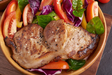 Grilled steak with fresh vegetable, sweet pepper, tomatoes, red onion, pink pepper and spices. Home made tasty food. Concept for tasty and healthy meal. Black stone background. Pork steak with salad