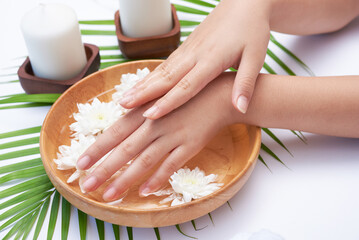 Woman soaking her hands in bowl of water and flowers, Spa treatment and product for female feet and hand spa, massage pebble, perfumed flowers water and candles, Relaxation. Flat lay. top view.
