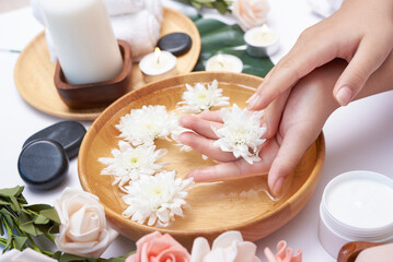 Woman soaking her hands in bowl of water and flowers, Spa treatment and product for female feet and hand spa, massage pebble, perfumed flowers water and candles, Relaxation. Flat lay. top view.