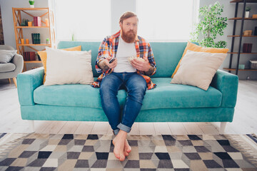 Obraz premium Bearded man in casual attire enjoying leisure time with snacks and television in a cozy living room at home