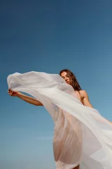 A sheer veil billows dramatically in the wind as a woman holds it high against a bright blue sky. A minimalist visual of grace and movement. © Yevhenii