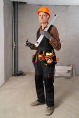 Elderly builder with tool belt holding wall measuring level and pencil looking at camera kindly. House construction and renovation