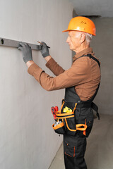 Elderly male builder using spirit level checking the leveling of a wall. Profession, construction and building