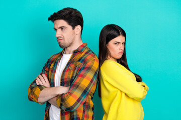 Young couple standing back-to-back with crossed arms on a teal background showcasing relationship...