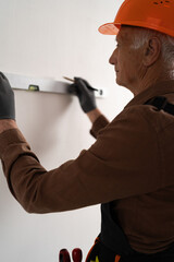 Retired Builder using a spirit level measuring wall in new house after renovation. Vertical view.
