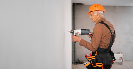 Professional builder or handyman in hardhat using a drill drilling hole in the wall