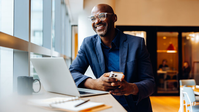 Professional man smiling while working on a laptop and holding a smartphone
