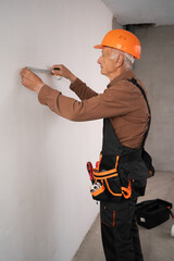 Building professional elderly builder during wall measurement in unfinished residential house using soft meter