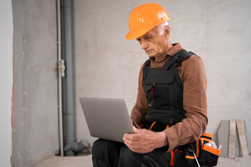 Elderly builder or civil engineer with a laptop working indoors new house. Architect or engineer are designing buildings.