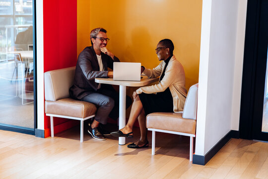 Two professionals discussing ideas on a laptop in a bright office booth