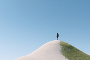 Obraz premium single figure triumphantly stands atop smooth featureless hill under expansive blue sky