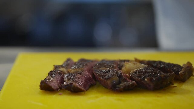 A man is cutting a piece of meat on a yellow cutting board. He is wearing a silver ring on his finger