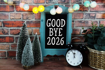 Goodbye 2026 text on blackboard easel stand with alarm clock on wooden and old brick wall background