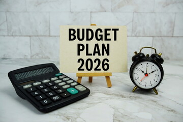 Budget plan 2026 text written on paper card with calculator and alarm clock on marble background