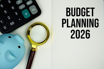 Budget Planning 2026 text on note page with calculator, piggy bank and magnifying glass