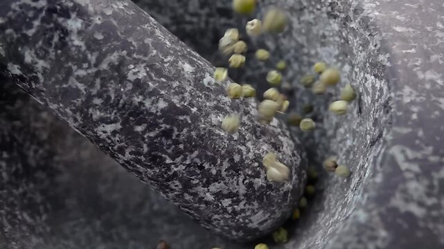 Close-up of the spicy green peppercorns falling into the grey stone mortar in slow motion