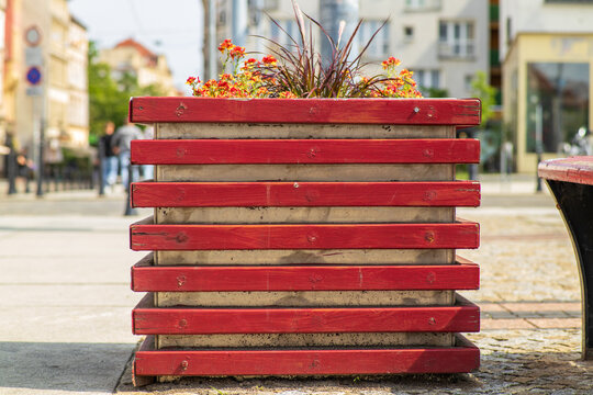 Red wooden flower planter with vibrant orange and purple flowers on a city street.
