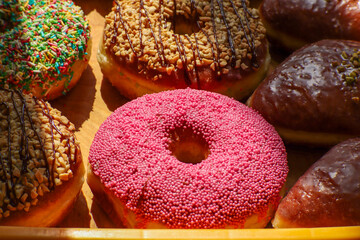 Colorful pink donut with tiny sprinkles on a wooden tray surrounded
