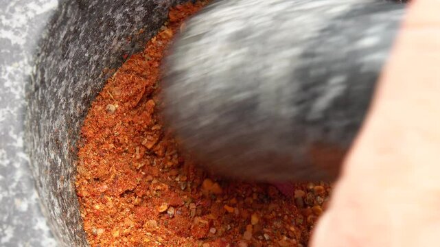 Super close-up of a pestle grinding and mixing various kinds of spices, peppers and sea salt in the grey stone mortar