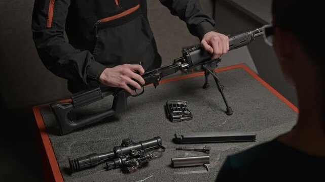 Cropped shot of specialist disassembling rifle on details while having practice with female trainee in shooting club