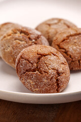 Festive ginger snap cookies in beige ceramic plate on wooden table close up