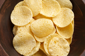 Salty fried high calorie potato chips in wooden bowl. Top view. 