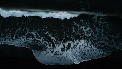 Dark and dramatic sea with powerful waves crashing against the black sandy beach seen from above