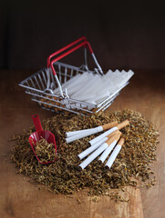 Tobacco heap with cigarettes, pile of tubes for make own cigarettes in a shop basket - concept about the underground cigarettes manufacture, counterfeit or alternative of legal tobacco products.