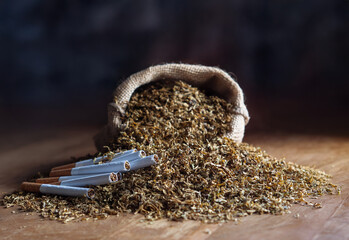 Tobacco sack with heap and few cigarettes on the table, closeup view, soft blur background. Roll-your-own  cigarettes manufacture or making cheaper cigarettes for self.