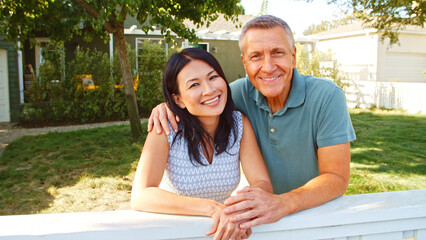 Portrait Of Smiling Mature Couple At Home Looking Over Back Yard Fence