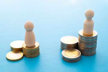 Concept of unequal pay in the workplace between men and women. Wooden figures on piles of coins.