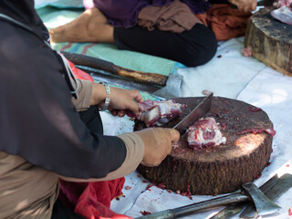 A group of women are cutting a pile of goat meat on a wooden tray with a knife during the Eid al-Adha celebration.  The butcher cuts raw goat meat with a knife. Ied al adha concept.