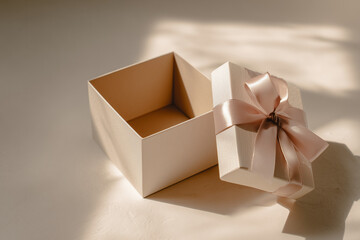 An open, empty gift box with a satin ribbon lid placed beside it on a clean, neutral surface. Soft lighting casts gentle shadows. The composition leaves generous copy space on the right side.