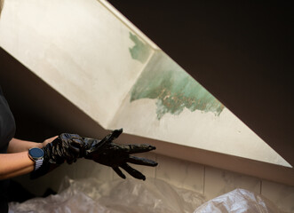 Close-up of a woman putting on black protective gloves before renovation work near an attic window....