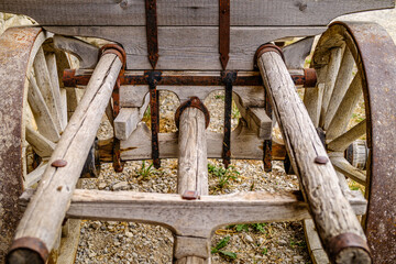 Vintage wooden cart with large wheels resting on a dusty floor in a rustic barn environment during the late afternoon light